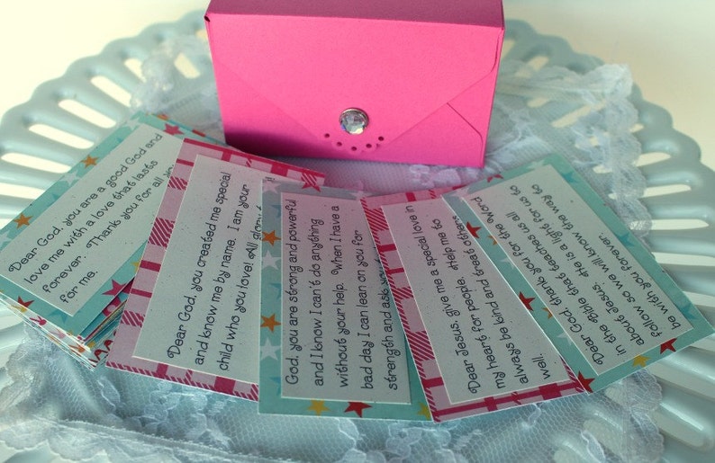 Puede incluir: Una pila de peque&ntilde;as tarjetas coloridas con mensajes inspiradores sobre Dios y Jes&uacute;s. Las tarjetas est&aacute;n decoradas con estrellas y patrones de cuadros. Las tarjetas est&aacute;n en una caja rosa.