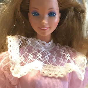 May include: A vintage Barbie doll with long blonde hair, wearing a pink sweater with a white lace collar.