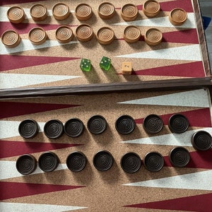 May include: A backgammon game board with brown and black checkers. The board has a cork surface with red and white triangles. There are two green dice and a single die with the number 2 on it.