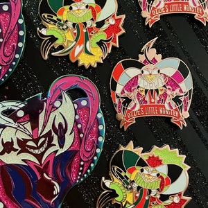 May include: Enamel pins featuring colorful cartoon characters with intricate designs. The pins showcase a variety of shapes and vibrant colors, including red, green, yellow, and black. Some pins have the text "Ozzie's Little Monster".