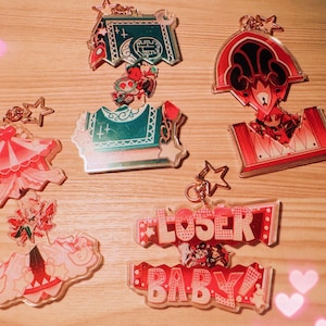 May include: A collection of acrylic keychains with various designs. The keychains feature red, pink, teal, and white colors. Some keychains have star-shaped attachments and the text "LOSER BABY!"