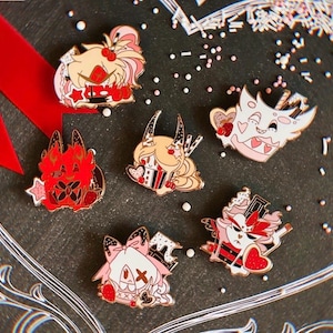 Puede incluir: Una colección de cinco pines de esmalte con personajes de dibujos animados estilizados en paletas de colores rojo, rosa y blanco. Cada pin muestra diseños únicos con motivos de corazones, detalles de chocolate y formas de estrellas, representados en un estilo gráfico plano con contornos marcados y colores sólidos.