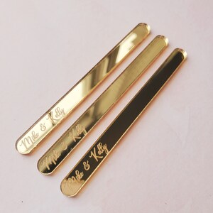 May include: Three gold-colored acrylic sticks with rounded ends. Each stick has the text "Mike & Kelly" engraved on it.