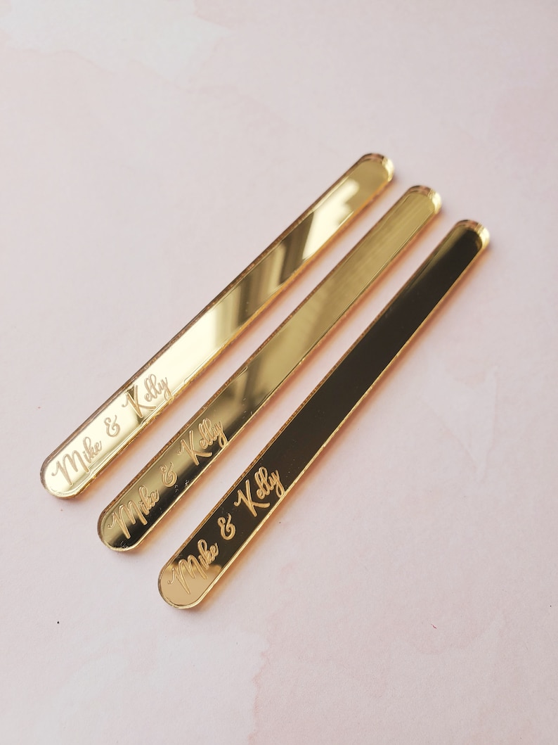 May include: Three gold-colored acrylic sticks with rounded ends. Each stick has the text "Mike & Kelly" engraved on it.
