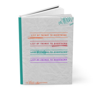 May include: A white notebook with a teal spine and a gray cover. The cover has the text "LIST OF THINGS TO OVERTHINK" written in orange, red, green, and purple.