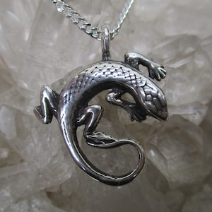 May include: A silver lizard pendant with a detailed textured design. The pendant is hanging from a silver chain.