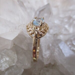 May include: A gold ring with a delicate filigree design and a light blue gemstone.
