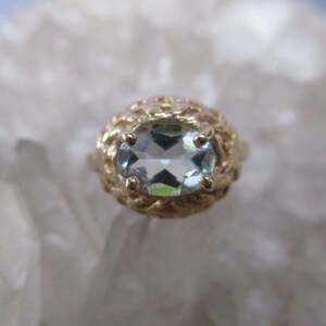 May include: A gold ring with a light blue oval-shaped gemstone set in a delicate, intricate design.
