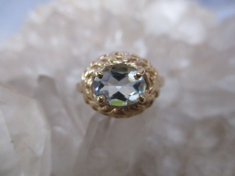 May include: A gold ring with a light blue oval-shaped gemstone set in a delicate, intricate design.
