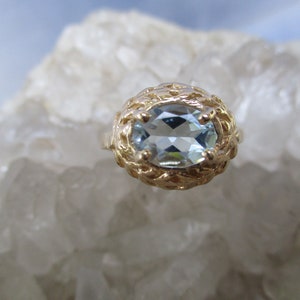 May include: A gold ring with a light blue oval aquamarine gemstone set in a delicate filigree design.