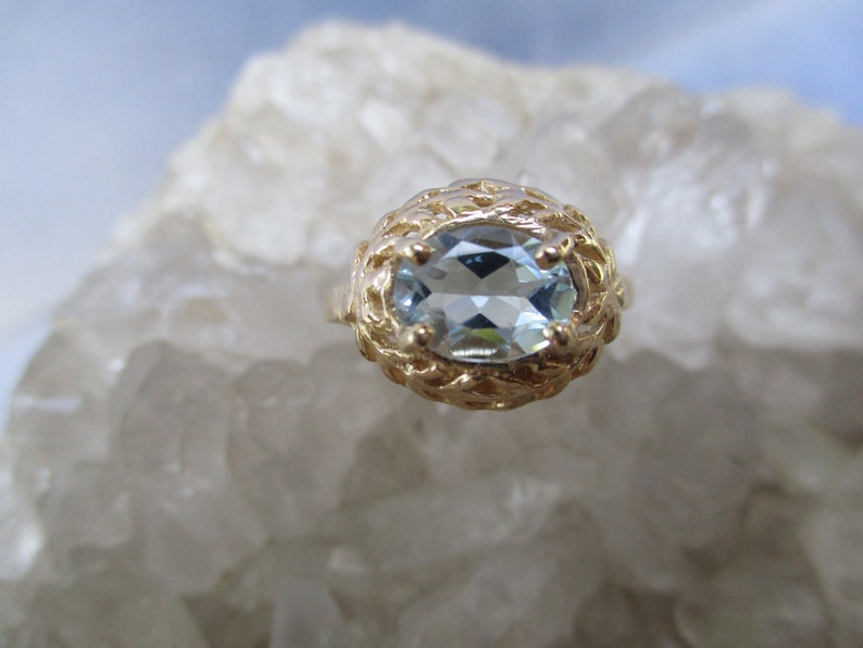 May include: A gold ring with a light blue oval aquamarine gemstone set in a delicate filigree design.