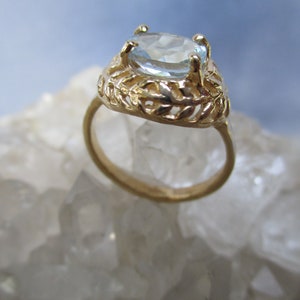 May include: A gold ring with a light blue oval gemstone set in a delicate, leafy design.