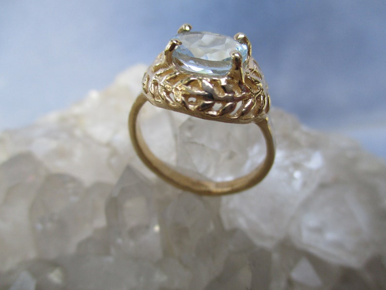 May include: A gold ring with a light blue oval gemstone set in a delicate, leafy design.