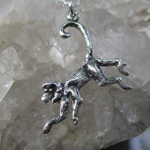 May include: A silver monkey charm pendant with a detailed design. The monkey is depicted in a playful pose, with its tail curled up and its arms outstretched.