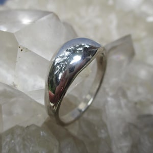 May include: A polished silver ring with a smooth, curved design. The ring reflects the surrounding light, creating a bright, shiny appearance. This piece of jewelry is a simple yet elegant accessory.