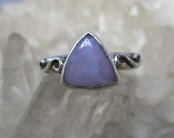 May include: A sterling silver ring featuring a triangular, pale lavender gemstone. The ring's band has a decorative, swirling design on each side of the gemstone. The gemstone is set in a silver bezel.