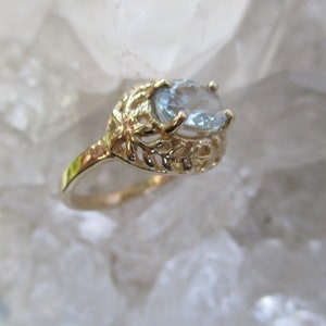 May include: A gold ring with a delicate, leafy design and a light blue oval gemstone.