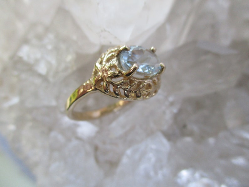 May include: A gold ring with a delicate, leafy design and a light blue oval gemstone.