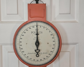 May include: A vintage wall-mounted American Family Scale with a coral-colored metal frame and a circular white face. The dial displays measurements up to 60 pounds, with black text reading 60 POUNDS, Patented Oct 24 1911, and American Family Scale.