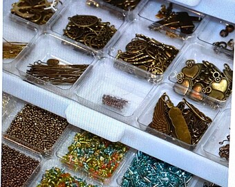 May include: A clear plastic storage box with multiple compartments filled with various small metal charms, beads, and findings. The box is organized with different types of embellishments, including hearts, stars, and geometric shapes.
