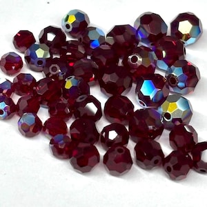 May include: A collection of faceted, deep red beads with iridescent highlights. The beads vary in size and shape, reflecting light with a shimmering effect. These beads are suitable for jewelry making and crafting projects.