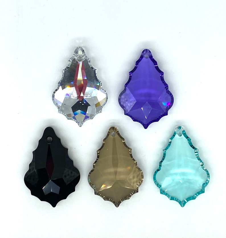 Op de afbeelding: Vijf kristallen druppelhangers in verschillende kleuren, waaronder helder, zwart, paars, bruin en blauw.