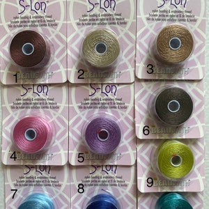 May include: Ten spools of S-Lon nylon beading and embroidery thread, each in a different color, labeled with numbers 1 through 10. The spools are packaged in clear plastic containers with pink and white labels.