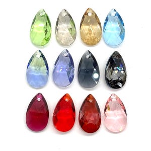 May include: A collection of twelve faceted, pear-shaped crystal pendants arranged in three rows. The colors include lime green, clear, gold, light blue, periwinkle, lavender, grey, black, magenta, bright red, dark orange, and pale pink.