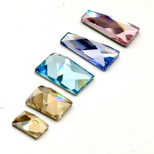 May include: Assortment of six rectangular iridescent glass rhinestones in various colors, including light blue, dark blue, pink, and gold.