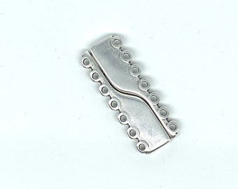Op de afbeelding: Een zilverkleurige rechthoekige sieradensluiting met een gebogen midden en meerdere kleine gaatjes langs de randen. De sluiting is ontworpen om twee sieraden te verbinden. De achtergrond is wit.