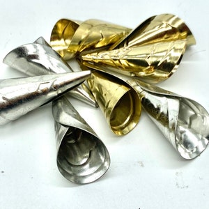 May include: A collection of metallic cone-shaped objects, some silver and some gold, are arranged against a white background. The cones have a rolled, petal-like appearance at their open ends, and a pointed tip. The metal has a slightly textured surface.