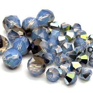 May include: A collection of faceted beads in various sizes and shades of blue, with hints of iridescent and metallic finishes. These beads are ideal for jewelry making and crafting projects.