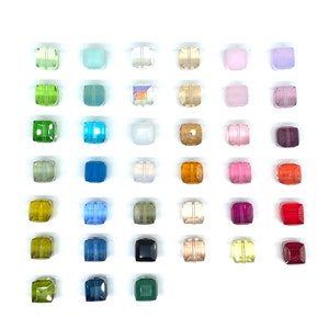 May include: Assortment of 36 square glass beads in various colors, including clear, green, blue, pink, purple, red, and orange. The beads are arranged in rows on a white background.