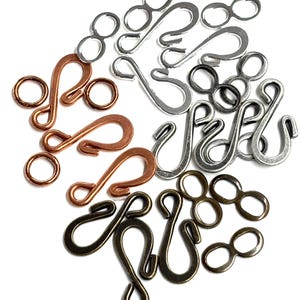 May include: Assortment of metal jewelry findings, including S-hooks and figure-eight connectors, in copper, silver, and antique brass finishes. These components are used for crafting necklaces, bracelets, and other jewelry projects. The findings are displayed against a white background.