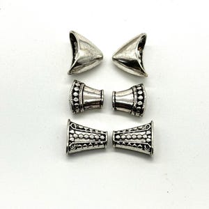 May include: Six silver metal end caps for jewelry making. The end caps have a textured design and are in the shape of a cone.