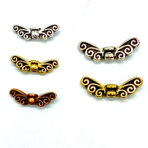 May include: Four pairs of decorative metal wings with a swirl design. The wings are in silver, gold, and bronze.