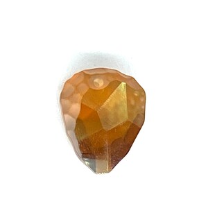 May include: A faceted teardrop-shaped crystal bead in gold and amber tones.