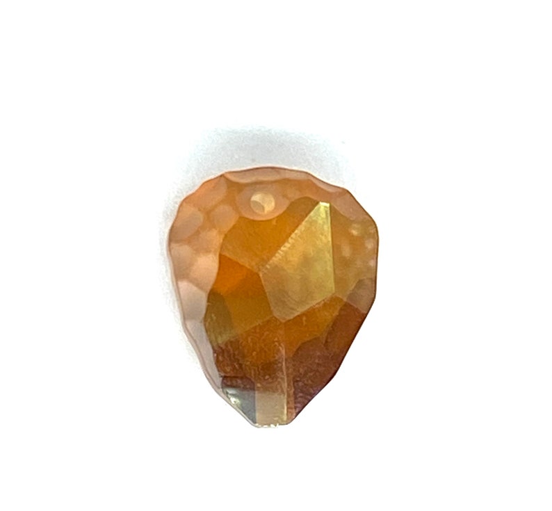 May include: A faceted teardrop-shaped crystal bead in gold and amber tones.