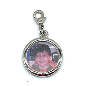 May include: Silver charm with a round photo frame featuring a picture of a young boy smiling. The charm has a silver clasp.