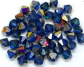May include: A collection of blue iridescent glass beads, each with a faceted, conical shape. The beads have a dark blue base colour with a rainbow iridescent finish.