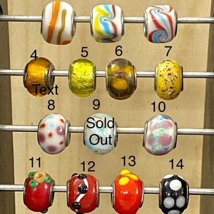 May include: A set of 14 colorful glass beads with various patterns and designs. The beads are arranged in rows on a metal rack. The beads are numbered 1 through 14. Some of the beads are sold out.