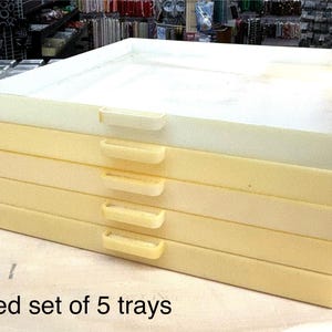 May include: A set of five white and cream colored plastic trays stacked on top of each other. The trays are used and have a slight yellowing to them.  Used set of 5 trays.