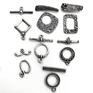 May include: A collection of silver-toned metal clasps and toggles for jewelry making. The clasps feature various designs, including circles, squares, and swirls.