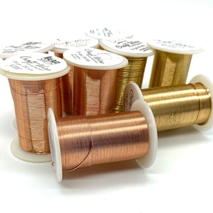 May include: Spools of copper and brass wire for jewelry making. The spools are labeled "Craft Wire" and have a white background with black text. The wire is wound around the spools and is visible in the image.