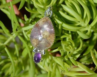 May include: A silver pendant with a teardrop-shaped clear stone with purple and brown inclusions. The pendant is accented with a smaller purple stone.