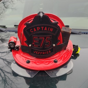 May include: Red fire helmet with a black leather patch that reads "Captain E75 Jeffries".