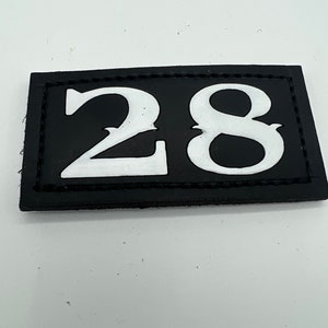 May include: Black leather patch with white stitching around the edges. The patch has the number 28 printed in white.