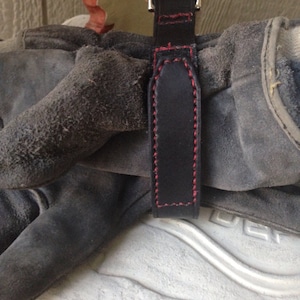 May include: A black leather strap with red stitching, attached to a pair of work gloves.