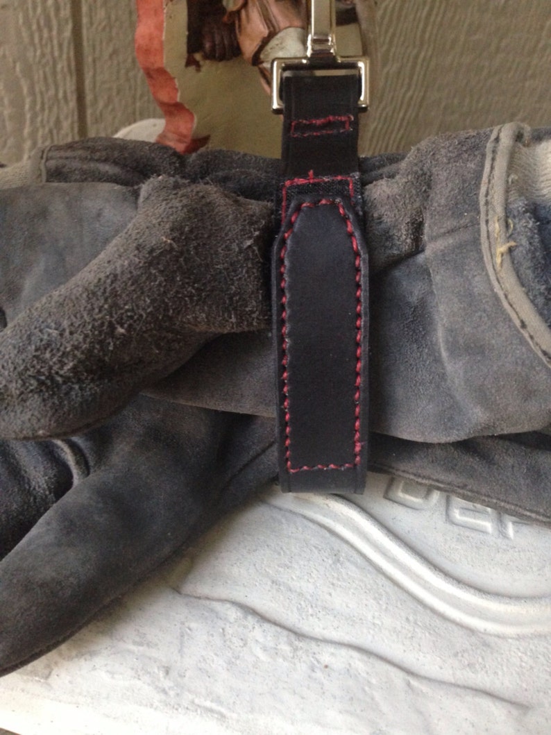 May include: A black leather strap with red stitching, attached to a pair of work gloves.