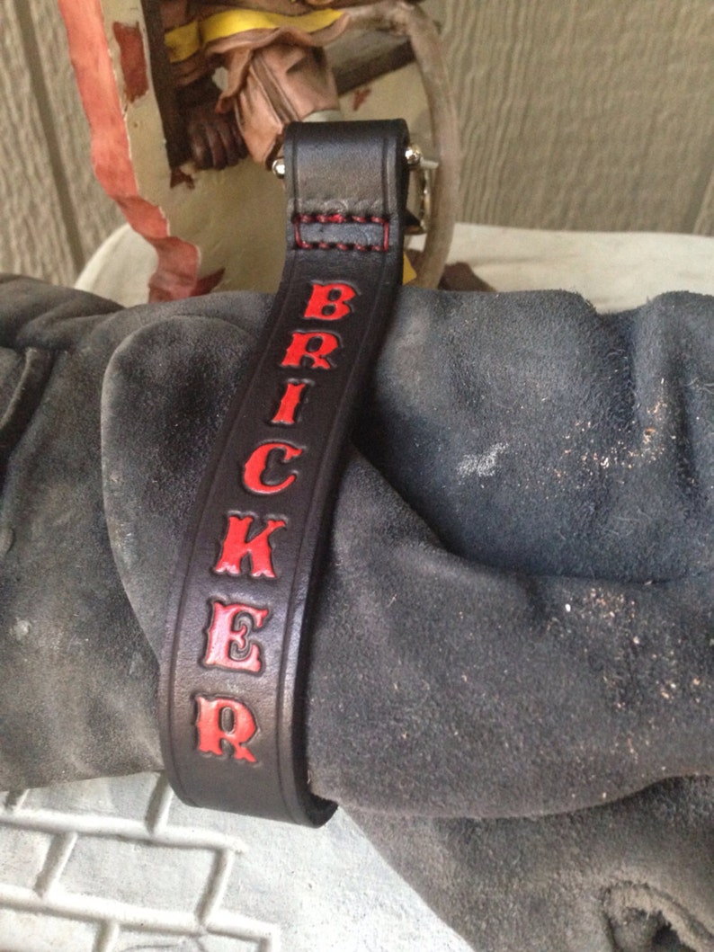 May include: Black leather strap with red stitching and the name "BRICKER" embossed in red letters.
